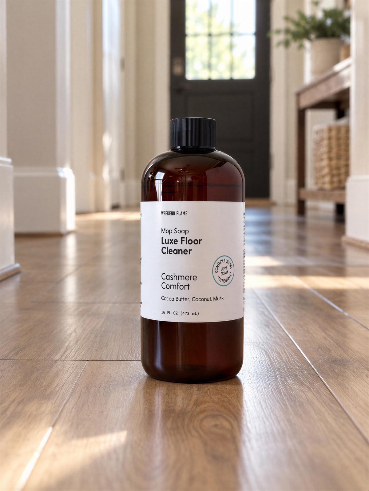A bottle of Luxe Floor Cleaner stands on a polished hardwood floor in a bright, modern room with natural light coming from a window in the background.