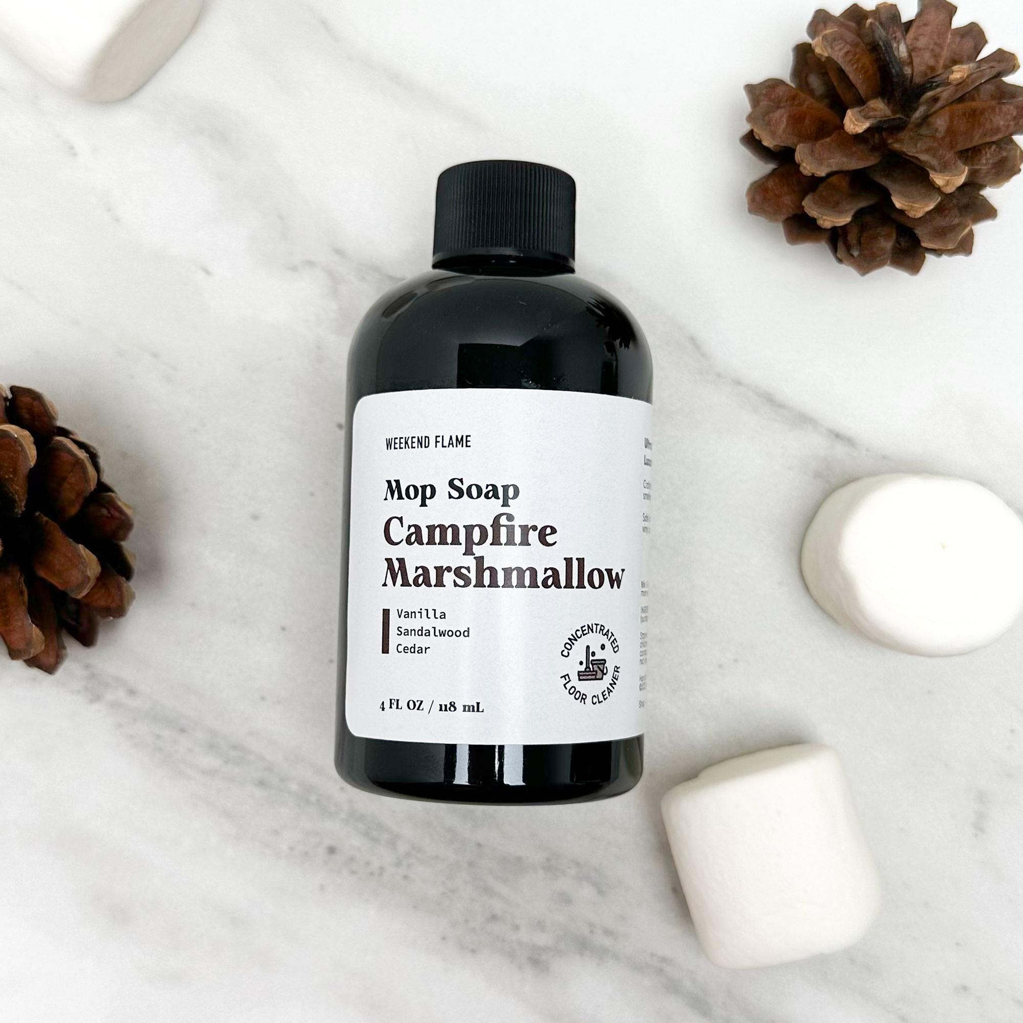 Trial size bottle of Mop Soap with Campfire Marshmallow scent on a marble surface with decorative elements.