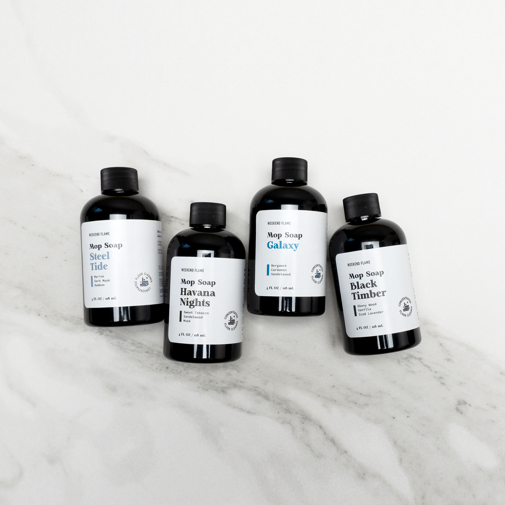 Four bottles of masculine soap labeled 'Steel Tide', 'Galaxy', 'Havana Nights', and 'Black Timber' on a marble surface.