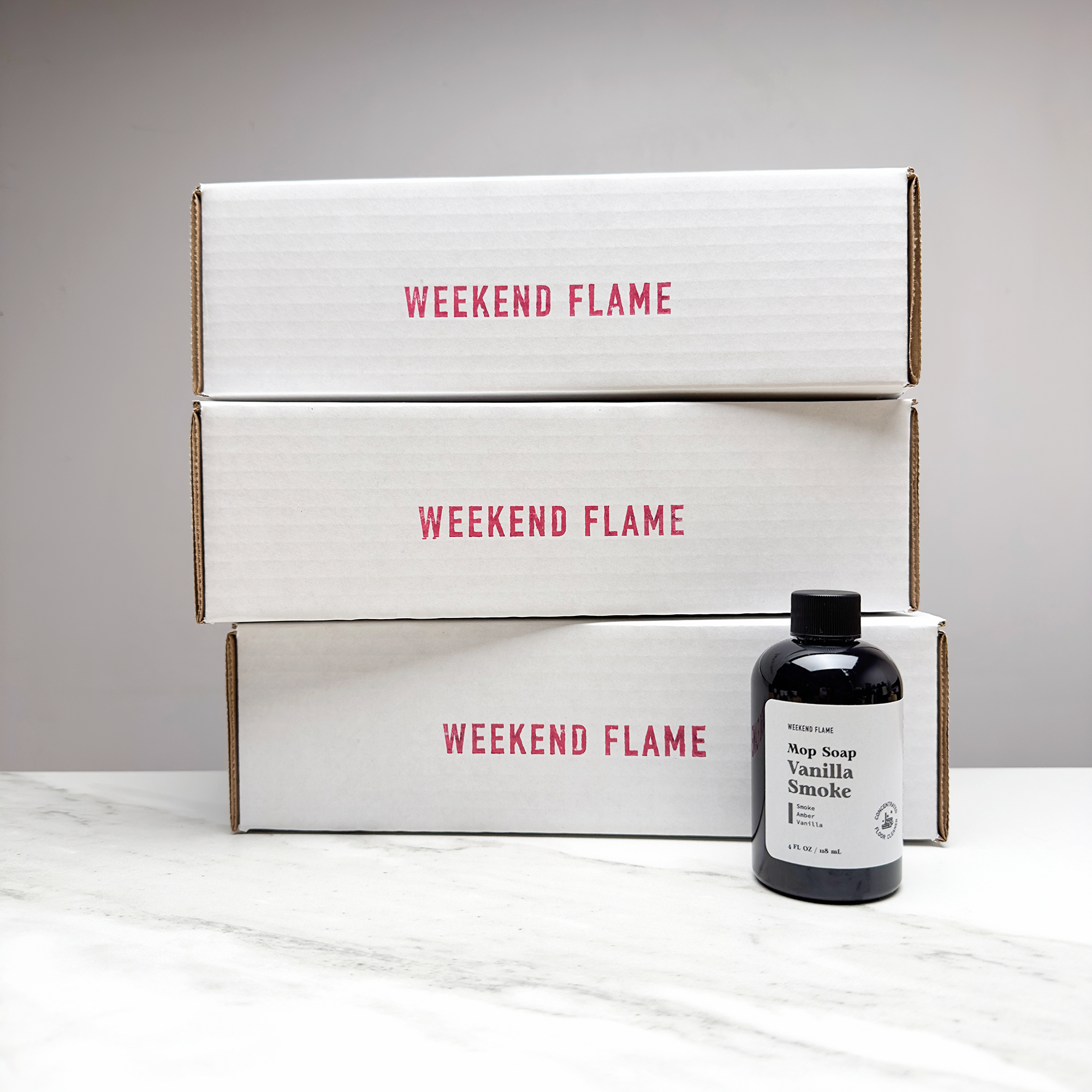 Three 'Weekend Flame' boxes with a bottle of mop soap on a light surface.