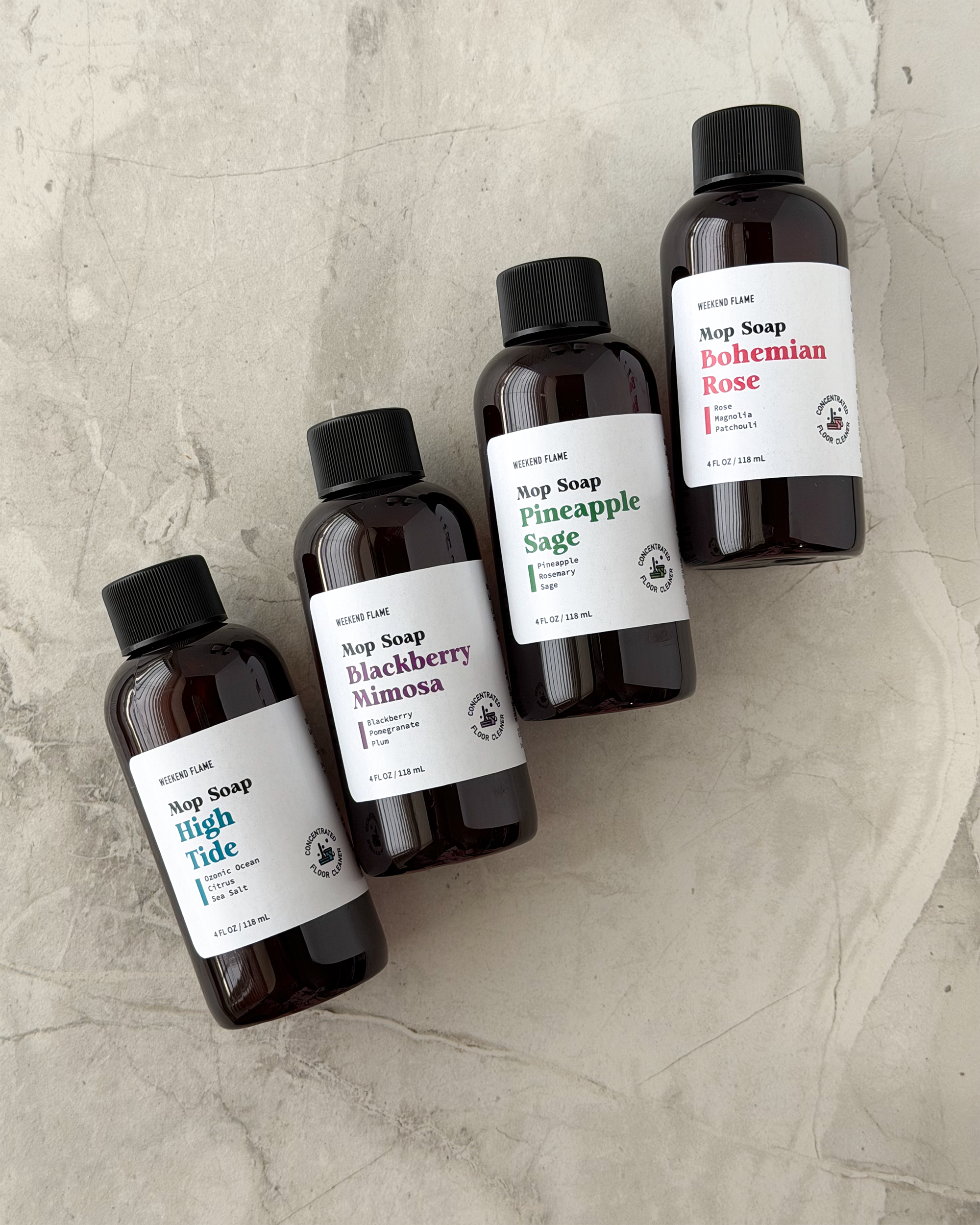 Four bottles of sample size soap with labels on a textured surface