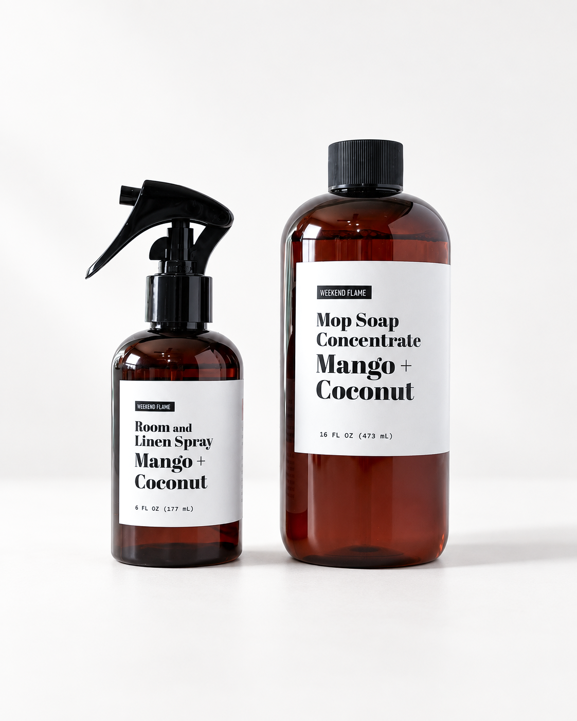 Two amber bottles with black caps and white labels on a clean white background. The larger bottle is labeled 'Mop Soap Concentrate Mango + Coconut' and the smaller bottle is labeled 'Room and Linen Spray Mango + Coconut'.