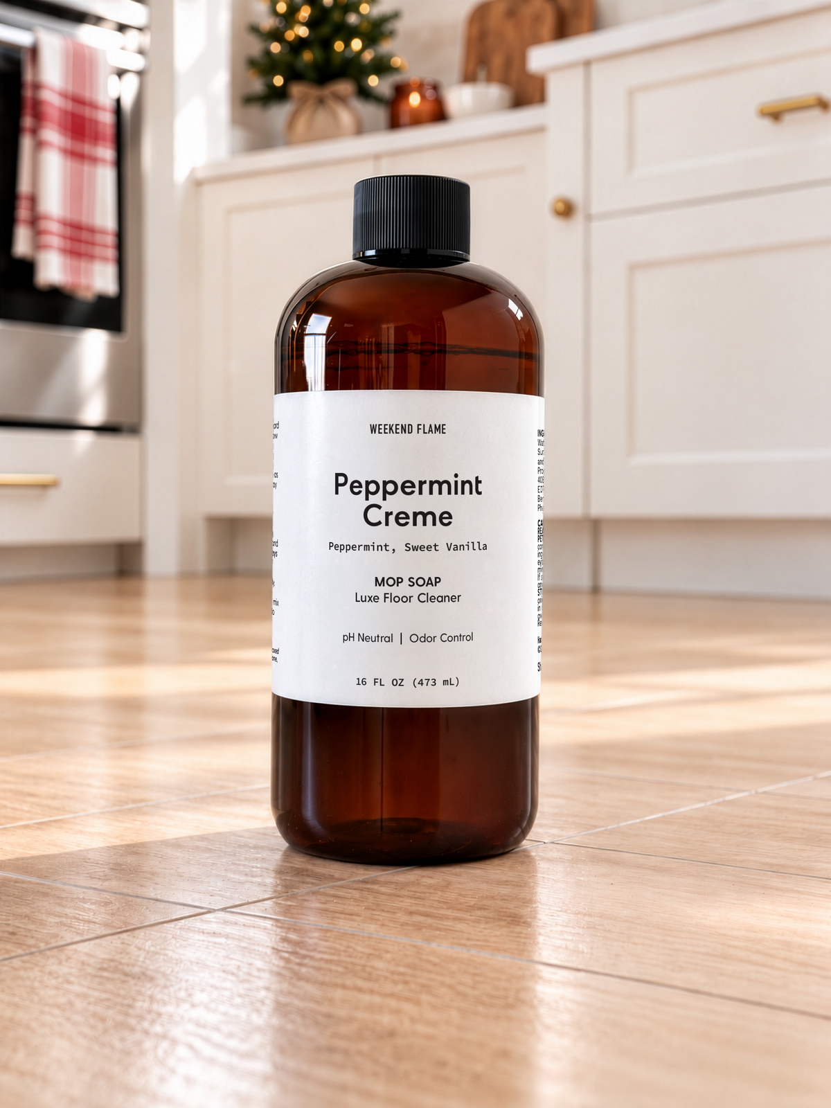An amber plastic bottle of Mop Soap Luxe Floor Cleaner in the Peppermint Creme scent, standing on a light wood floor in a bright, modern kitchen.