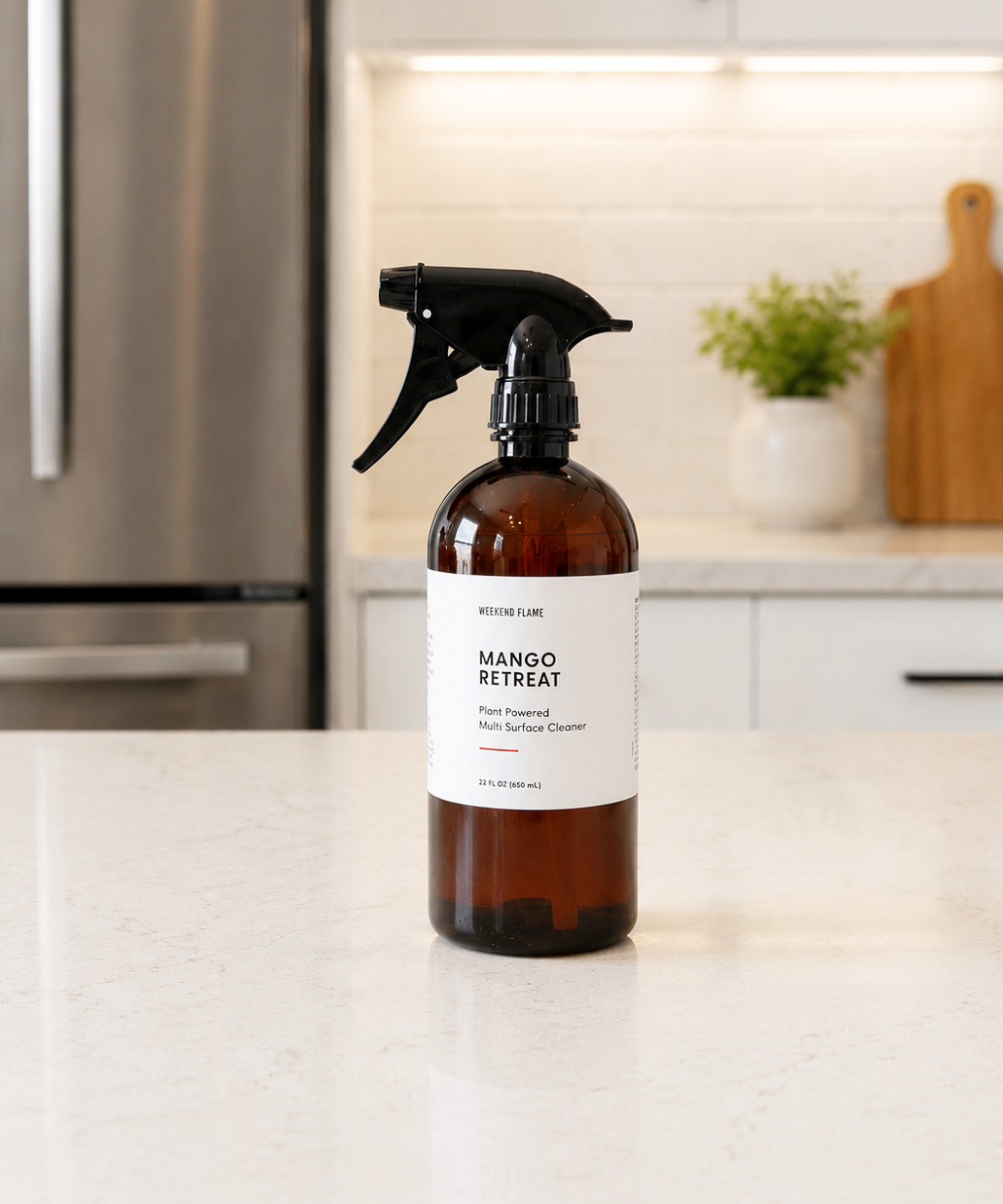 An amber plastic spray bottle of premium plant based multi surface cleaner, standing on a white kitchen countertop with a blurred modern kitchen background.