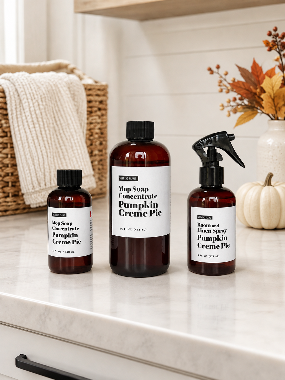 Pumpkin Creme Pie Mop Soap Concentrate and Room and Linen Spray in amber bottles displayed on a bright laundry room countertop with minimal fall decor and pumpkins