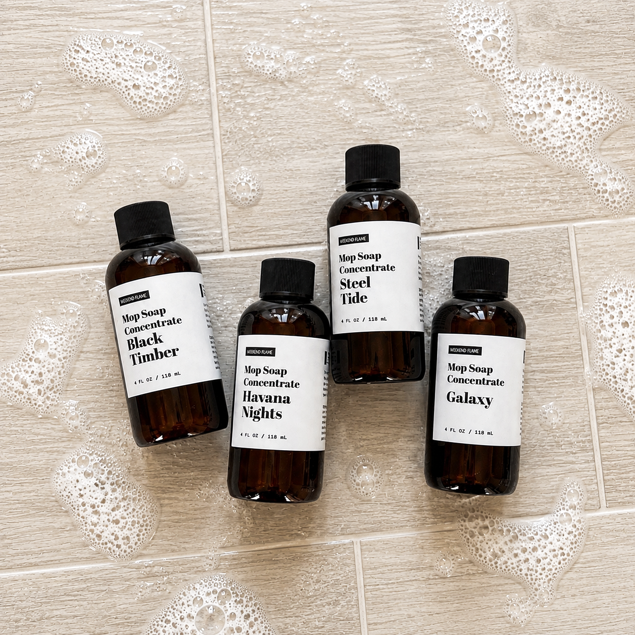 The Gentleman’s Collection trial size Mop Soap set featuring four 4 oz bottles in Galaxy, Havana Nights, Black Timber and Steel Tide, displayed on a lightly soapy tile floor.