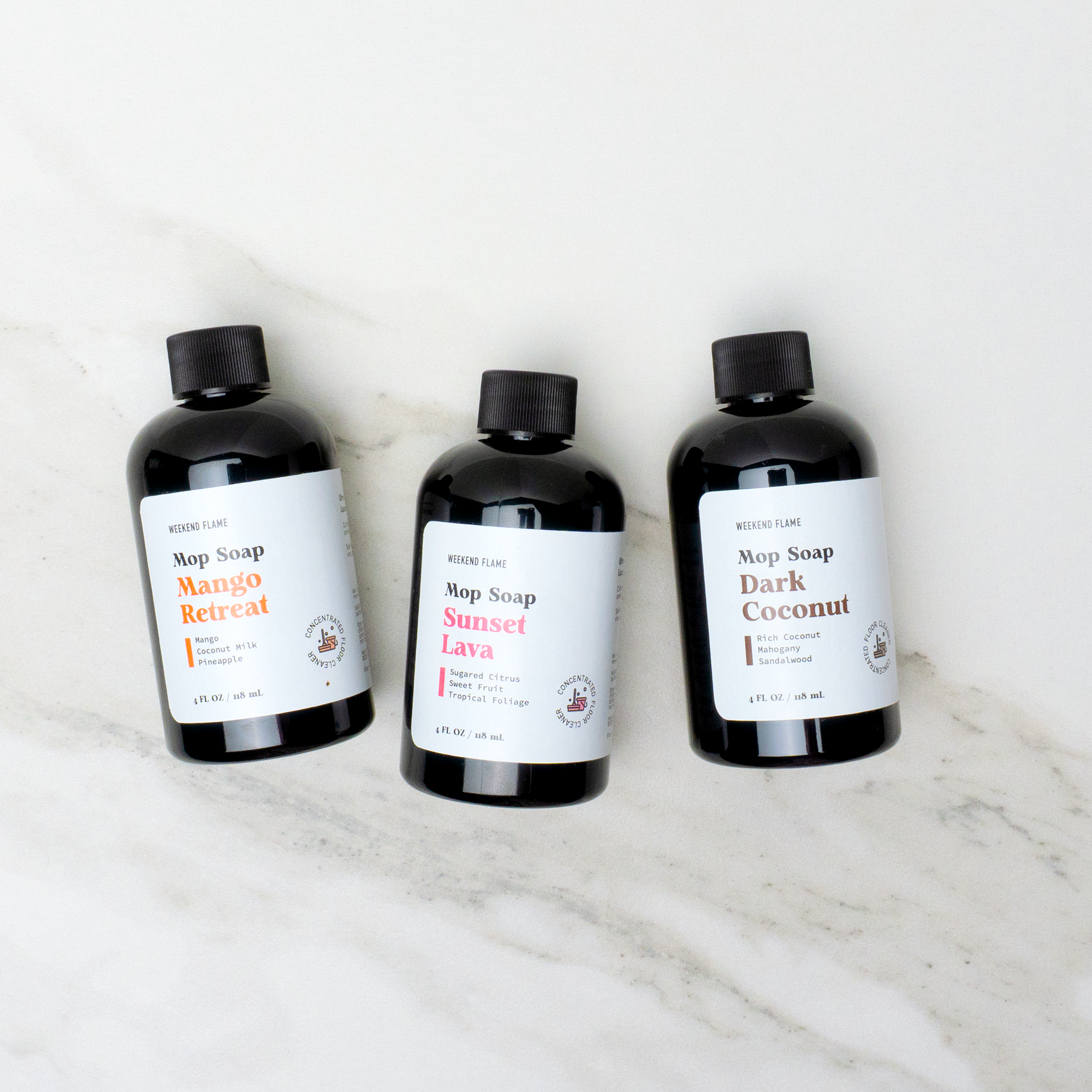 Three assorted bottles of scented mop soap in different fragrances, neatly arranged on a clean surface.